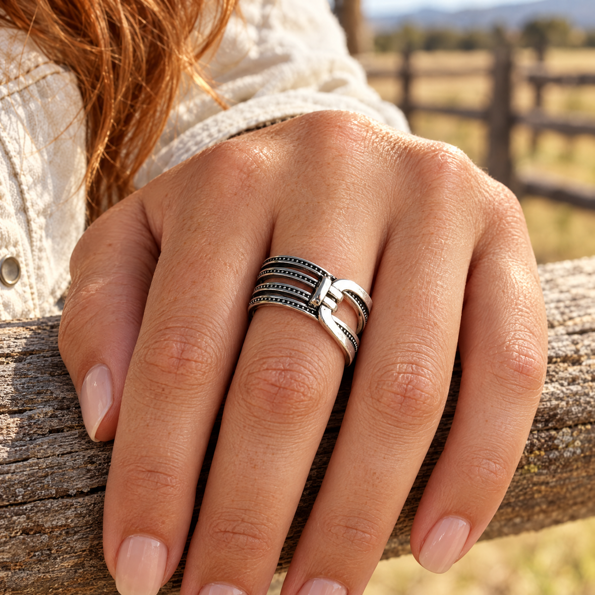 Saddle Cinch Ring worn on hand resting on a corral fence